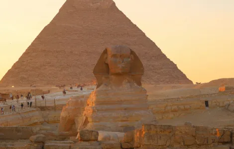 Vue emblématique du Grand Sphinx de Gizeh avec la Grande Pyramide en arrière-plan sous un ciel clair.