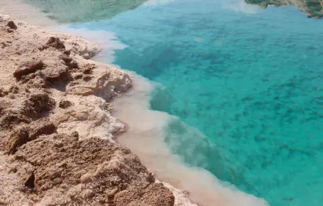 Gros plan sur les cristaux de sel blanc bordant une eau turquoise cristalline dans un lac salé à Siwa.