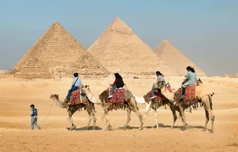 Voyageurs à dos de chameau dans le désert devant les pyramides d'Égypte avec l'agence Esquisse Voyage.