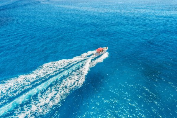 Motorboat at the sea in balearic islands. Aerial view of floating boat with people in transparent blue water at sunny day. Summer landscape. Top view from drone. Seascape with yacht in motion in bay