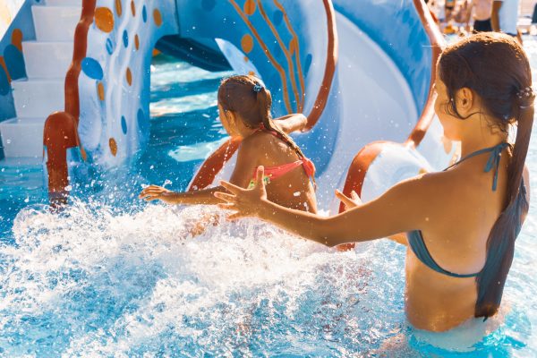 The cautious older sister catches her cute little one who slides down the slide right into the pool and splashes